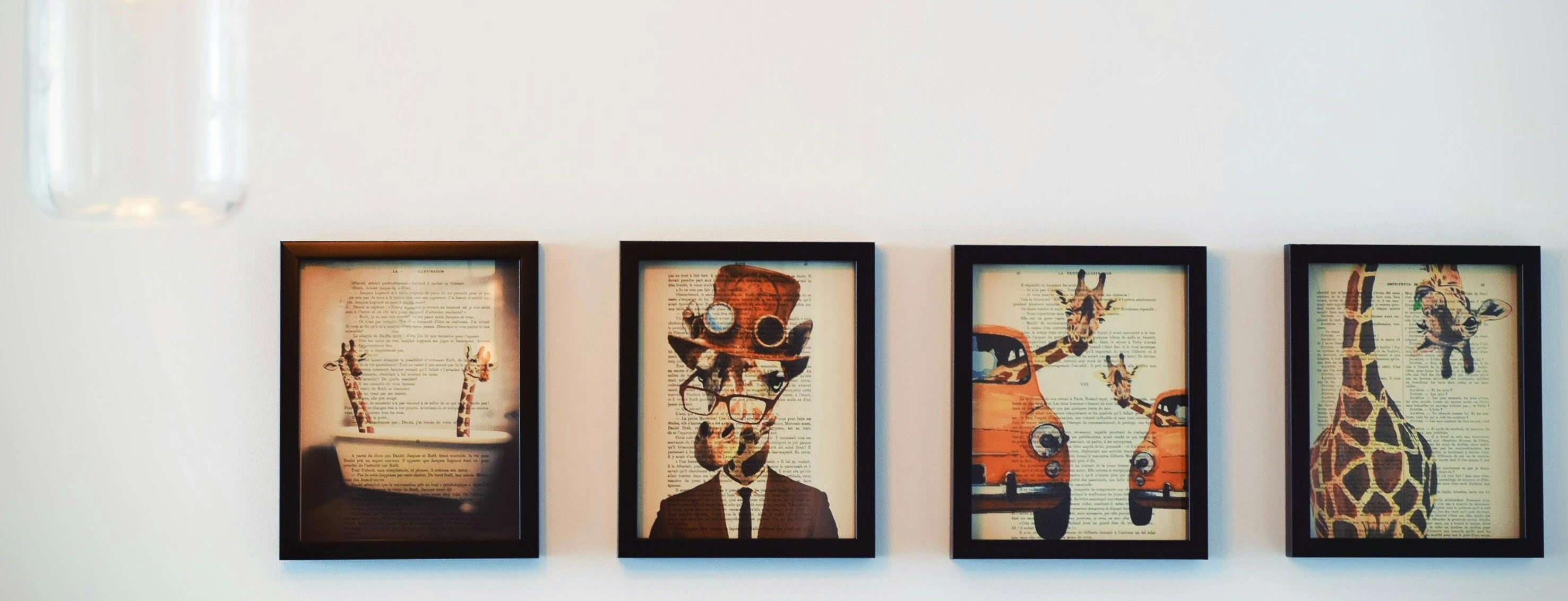 Four framed artworks of animals on a white wall with two pendant lights.